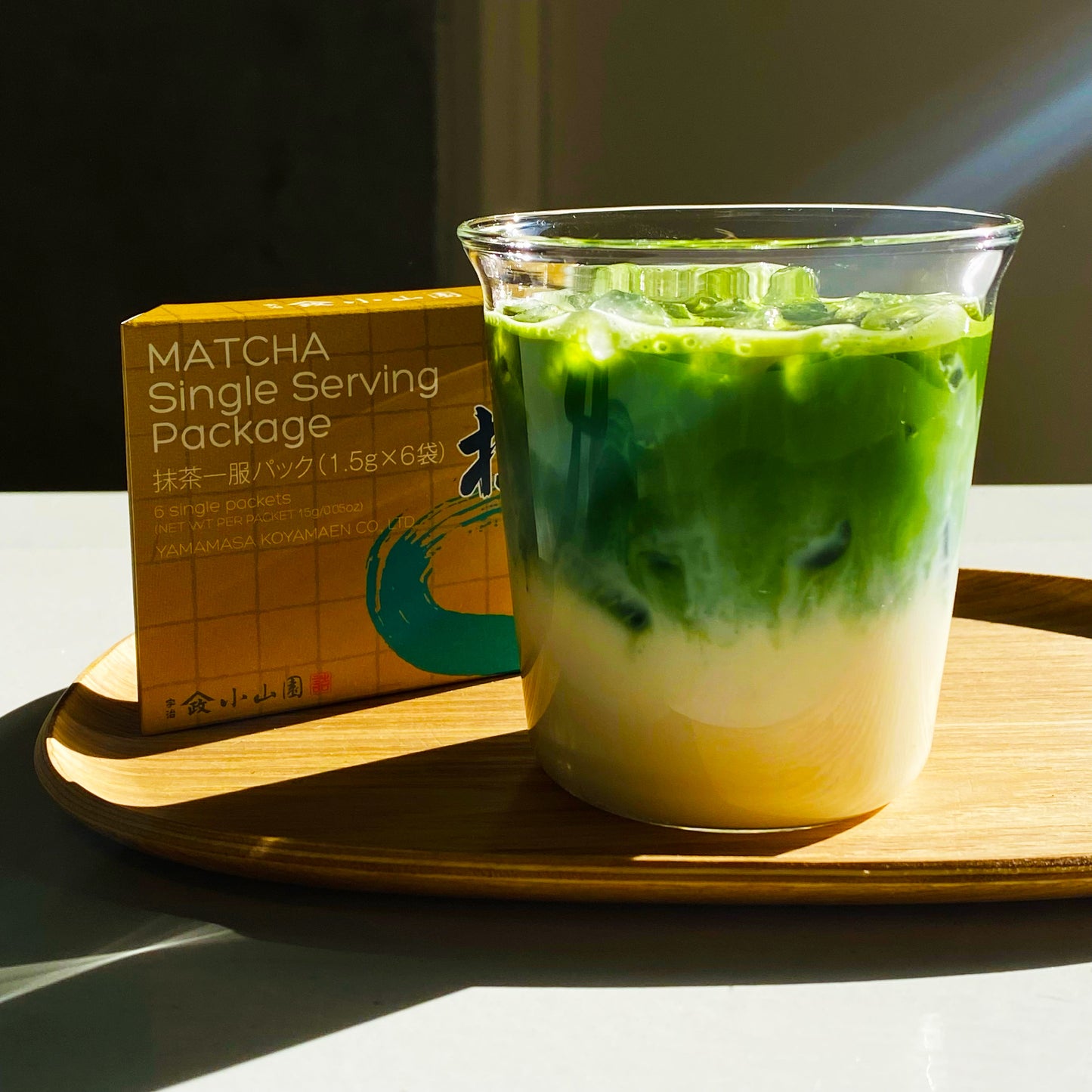Yamamasa Koyamaen latte in a clear cup with a matcha powder package on a wooden tray.