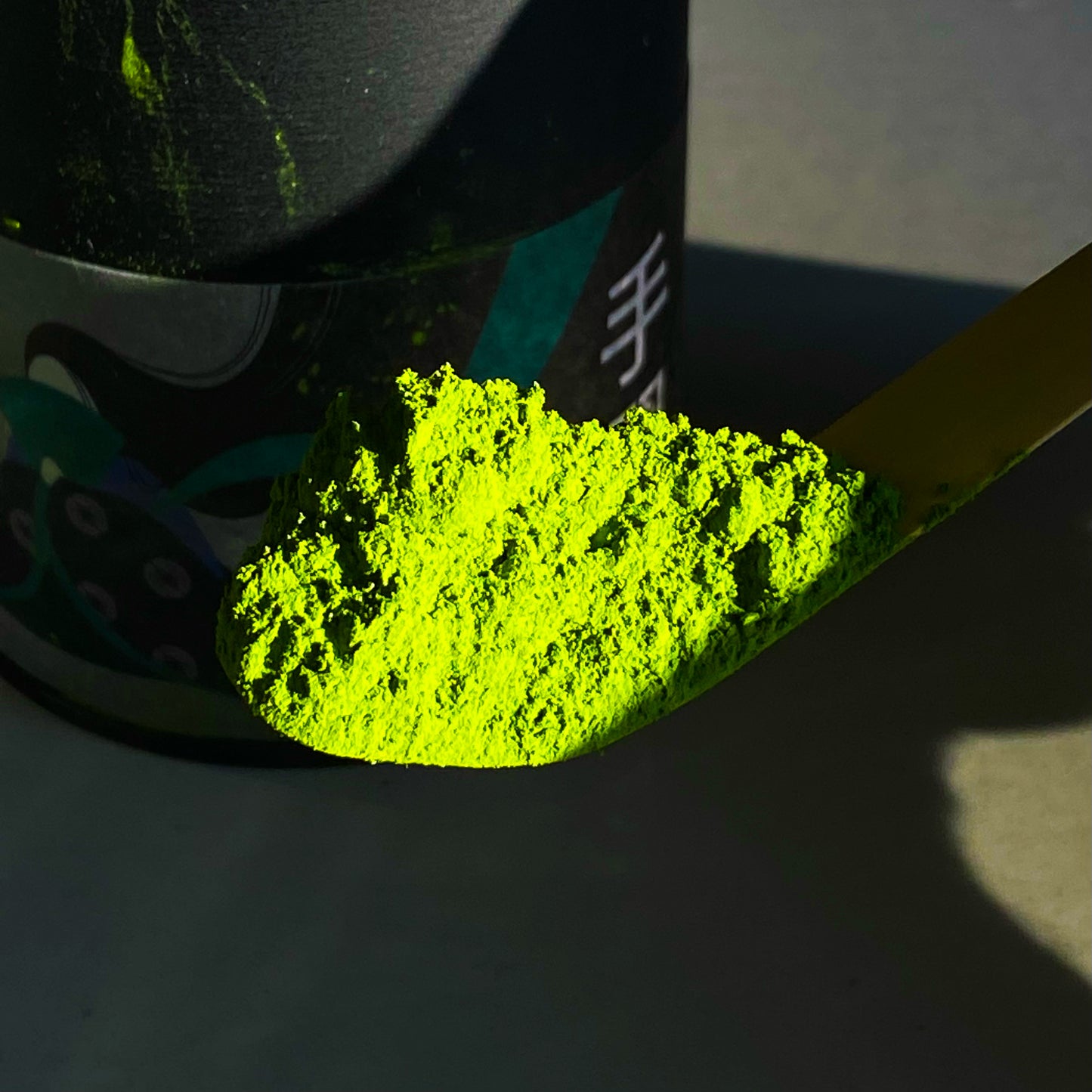 Tenarai Matcha powder on a bamboo scoop next to a can of Tenarai matcha powder.