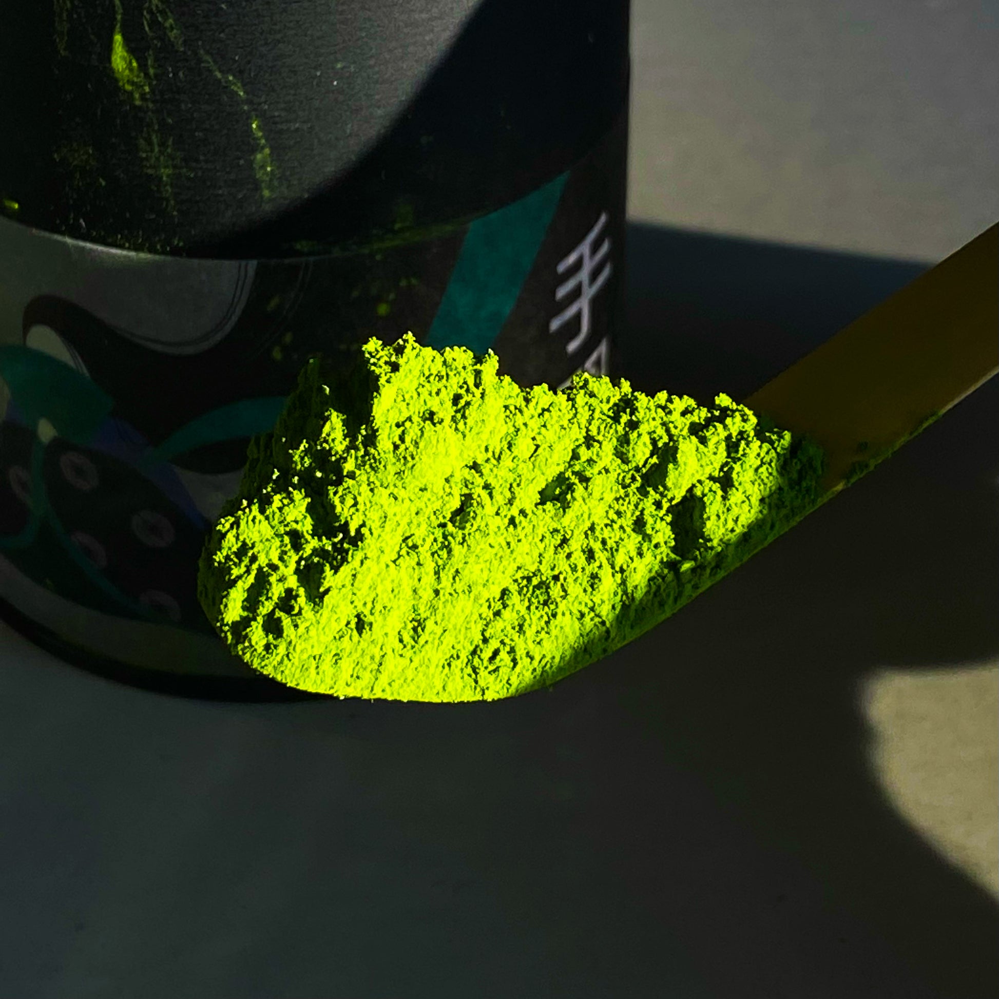 Tenarai Matcha powder on a bamboo scoop next to a can of Tenarai matcha powder.